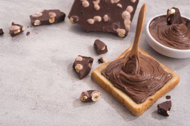 Çikolata, kaşıkla bir dilim ekmeğe, erimiş krema beyaz kâsesine ve taş bir masada fındıklı çikolataya sürüldü. Popüler tatlı yiyecekler.