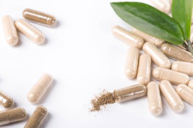 Beyaz arka planda yeşil yapraklı ilaç ve kapsül sürüsü.