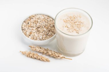 Beyaz arka planda izole edilmiş bir bardak yulaf sütü ve tahıl.