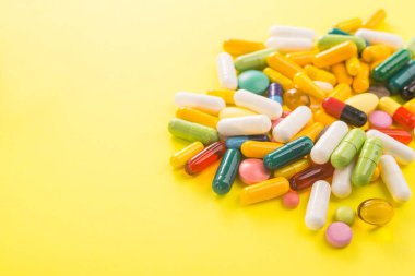 Sarı arka planda renkli kapsül hapları yığını. Parlak tıbbi fotoğraf.