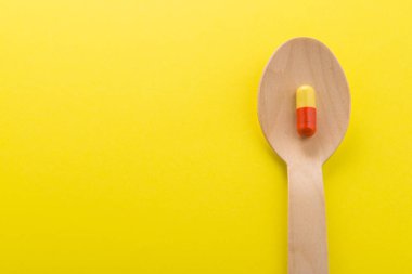 Bir süper kırmızı ve sarı kapsül kaşıkta, sarı arka planda. Minimalizm konsepti. Üst Manzara. Metin için boşluk.