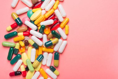 Renkli haplar, kapsül ve tabletler, pastel pembe arka planda. Üst Manzara. metin için yer.