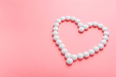 Beyaz kalp, tablet ve haplardan yapılmış pembe pastel arka planda