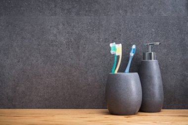 Tahta bir masada üç diş fırçası olan gri bir taş tutucu. İskandinav tuvaletindeki aksesuarlar. mesaj için yer. Boşluğu kopyala