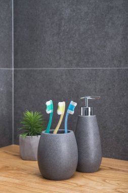 Tahta bir masada üç diş fırçası olan gri bir taş tutucu. İskandinav tuvaletindeki aksesuarlar..