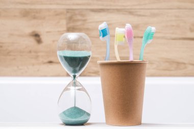 Banyoda kum saati olan kağıt bardakta dört diş fırçası. Hijyen ve diş temizliği.