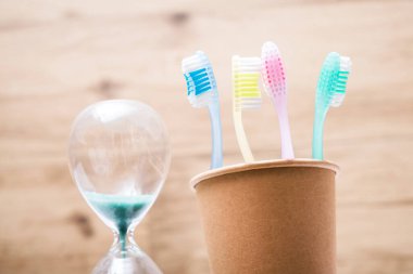 Banyoda kum saati olan kağıt bardakta dört diş fırçası. Hijyen ve diş temizliği.