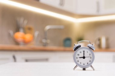 Kithen beyaz ahşap masadaki gri alarmlı saate odaklanmış. Kahvaltı vakti, sabah 9 'da..