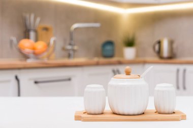 Beyaz bir masanın üzerinde beyaz porselen kaplar içinde şeker, tuz ve siyah biber baharatı, defocus mutfak arka planı karşı.