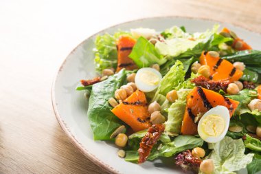 Beyaz tabakta kabaklı, yumurtalı, domatesli ve nohutlu taze salata. Vitamin gıda geçmişi.