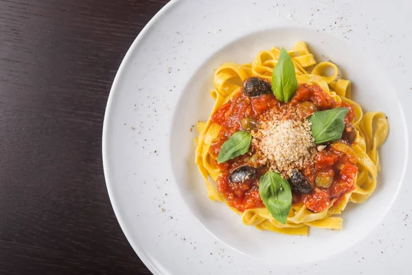 Beyaz tabakta domatesli, zeytinli ve fesleğenli İtalyan makarnası. popüler yemek