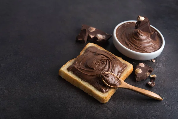 Çikolata, kaşıkla bir dilim ekmeğe, erimiş krema beyaz kâsesine ve taş bir masada fındıklı çikolataya sürüldü. Popüler tatlı yiyecekler.