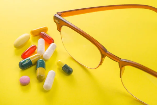 Old style glasses with vitamin and pills on a yellow background.