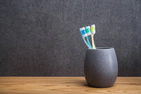 Tahta bir masada üç diş fırçası olan gri bir taş tutucu. İskandinav tuvaletindeki aksesuarlar. metin için yer