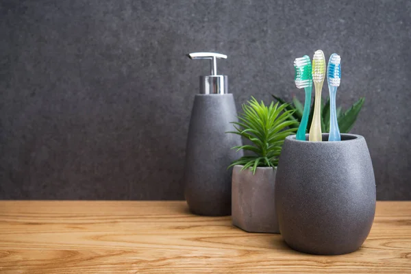 Tahta bir masada üç diş fırçası olan gri bir taş tutucu. İskandinav tuvaletindeki aksesuarlar..