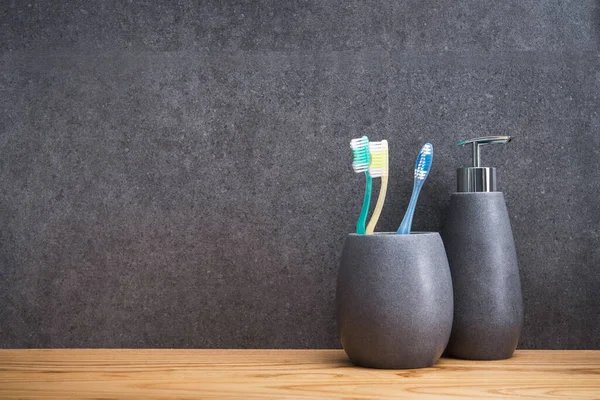 Tahta bir masada üç diş fırçası olan gri bir taş tutucu. İskandinav tuvaletindeki aksesuarlar. mesaj için yer. Boşluğu kopyala