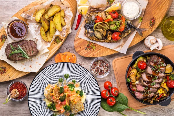 Tabaklarda biftek, tavada biftek, ahşap masada ızgara sebzeli uskumru. Üst Manzara. düz yat