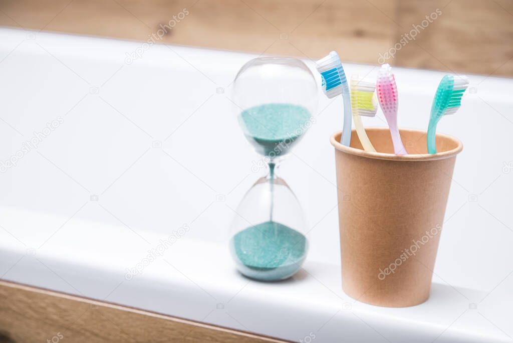 Four toothbrushes in a paper cup with hourglass in the bathroom. hygiene and teeth cleaning.