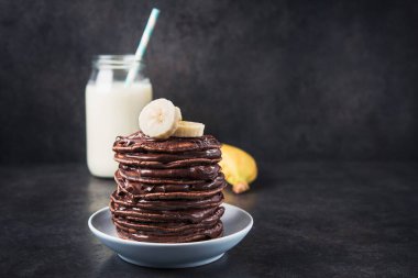 Taş bir masanın üzerinde çikolata, muz ve süt şişesi olan lezzetli bir krep. Yüksek kalorili kahvaltı..