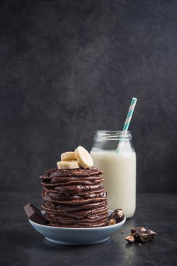 Taş bir masanın üzerinde çikolata, muz ve süt şişesi olan lezzetli bir krep. Yüksek kalorili kahvaltı..