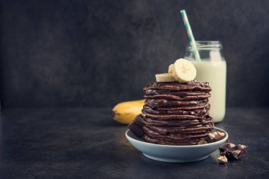 Taş bir masanın üzerinde çikolata, muz ve süt şişesi olan lezzetli bir krep. Yüksek kalorili kahvaltı..
