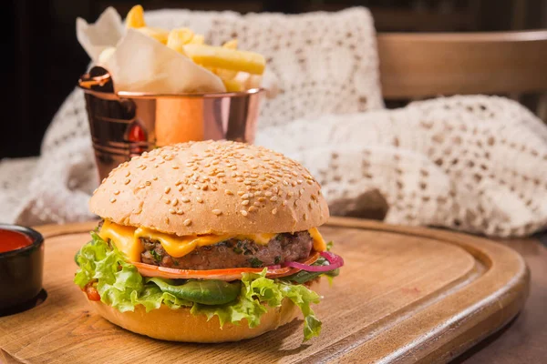 Tahtadan yapılmış lezzetli bir hamburger, yanında da çay tabağı ketçapı ve patates kızartması.