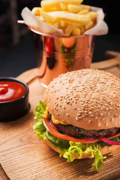 Tahtada lezzetli bir hamburger, yanında çay tabağı, ketçap ve patates kızartması.