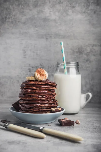 Taş bir masanın üzerinde çikolata, muz ve süt şişesi olan lezzetli bir krep. Yüksek kalorili kahvaltı..