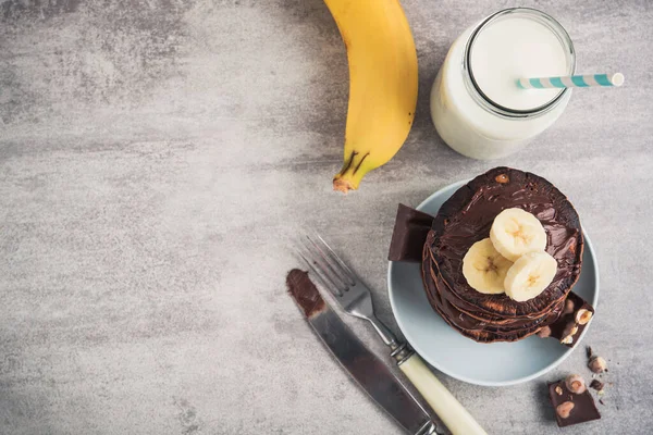 Taş bir masanın üzerinde çikolata, muz ve süt şişesi olan lezzetli bir krep. Yüksek kalorili kahvaltı. Yukarıdan görünüm