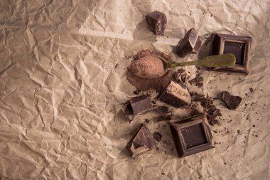 Büyük parça koyu çikolata ve eski kaşık kakao tozu, arka planda el işi kağıt. Üst Manzara. Boşluğu kopyala