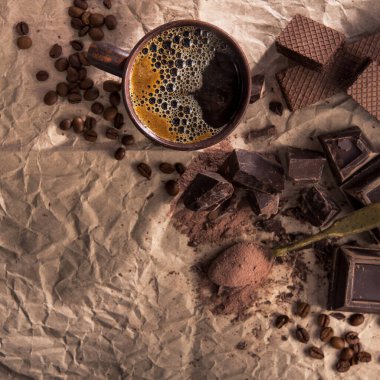 Büyük parça koyu çikolata, kakao tozu ve kağıt üzerinde kahve fincanı..