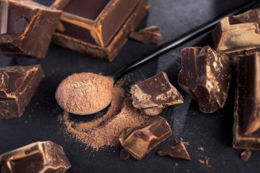 Büyük siyah çikolata parçaları ve siyah kaşıkta kakao tozu..