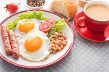 İngiliz kahvaltısı, kızarmış yumurta, fasulye, domates, sosis, taze marul yaprağı, kahve fincanı. Kırmızı yemek kavramı.