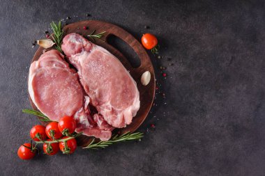 Ahşap bir tahtada çiğ domuz bifteği, baharatlar ve pişirmek için malzemeler. en üstteki görünüm.