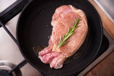 Kızarmış tavada biberiyeli domuz bifteği. Mutfakta ocakta et pişiriyorum..