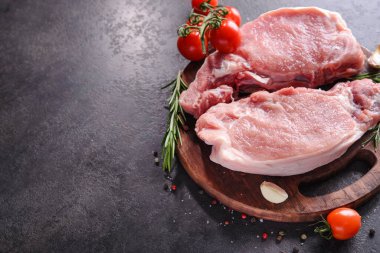 Ahşap bir tahtada çiğ domuz bifteği, baharatlar ve pişirmek için malzemeler. Metin için yer.
