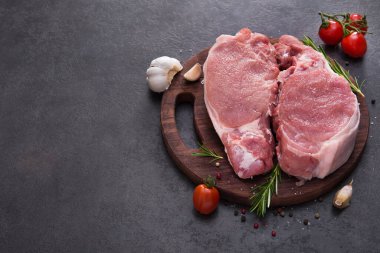 Ahşap bir tahtada çiğ domuz bifteği, baharatlar ve pişirmek için malzemeler. Metin için yer.
