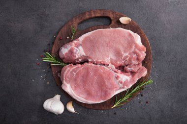 Ahşap bir tahtada çiğ domuz bifteği, baharatlar ve pişirmek için malzemeler. en üstteki görünüm.