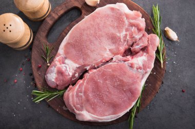 Ahşap bir tahtada çiğ domuz bifteği, baharatlar ve pişirmek için malzemeler. en üstteki görünüm.