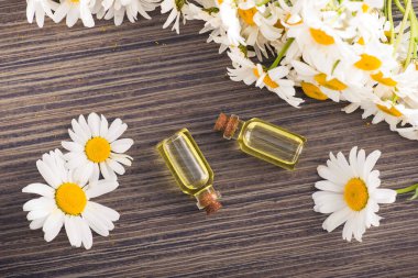 Cam şişe, ahşap bir masada çiçekli papatya yağı aromalı. Kozmetik ve tıbbi organik sıvı kavramı. en üstteki görünüm