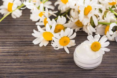 Masasında papatya kremi ve çiçek olan bir kap. kozmetik cilt ve vücut bakımı kavramı.