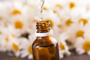 Cam şişe, ahşap bir masada çiçekli papatya yağı aromalı. Kozmetik ve tıbbi organik konsept.