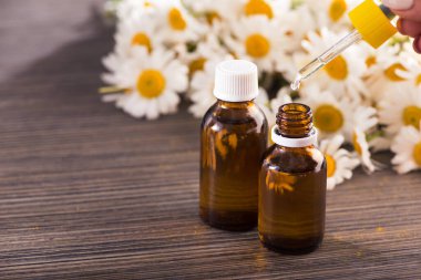 Cam şişe, ahşap bir masada çiçekli papatya yağı aromalı. Kozmetik ve tıbbi organik konsept.