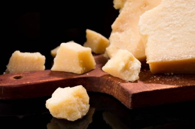 Parmesan peynirinin lezzetli ve taze parçalarını bölme tahtasında, siyah arka planda..