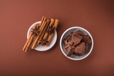 Çikolata ve baharatlı tarçın parçaları. Kahverengi arka planda beyaz kâsede beyazdı. Üst görünüm.