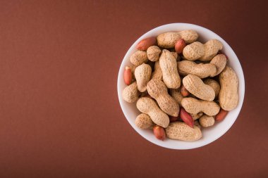 Kahverengi arka planda beyaz bir kasede organik fıstıklar. Üst Manzara. metin için yer