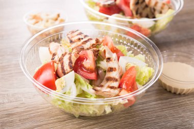 Ahşap zemin üzerinde taze salata olan plastik paket kutusu..