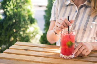 Genç ve güzel bir kız kafedeki ahşap masada soğuk içecek kokteyli içiyor. Yaz yaşam tarzı insanları.