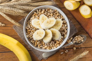 Tohum ve buğdaylı kasede gevrek gevrek, ahşap bir masada muz. Kaba, sağlıklı kahvaltılık mısır gevreği. en üstteki görünüm.