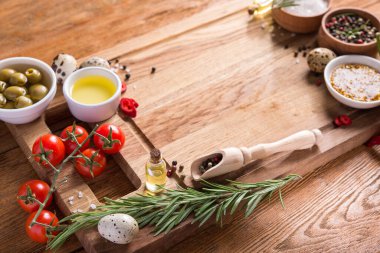 Taze salata malzemeleri (tuz, biber, zeytin, domates, biberiye, yağ) ahşap bir masa üzerinde kesim tahtasıyla birlikte.